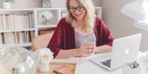 woman smiling holding glass mug sitting beside table with MacBook